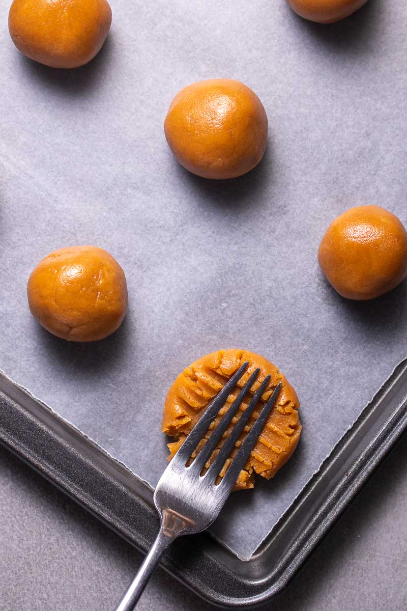 Pâte à biscuits roulée en boules sur une plaque à pâtisserie avec une fourchette aplatissant un