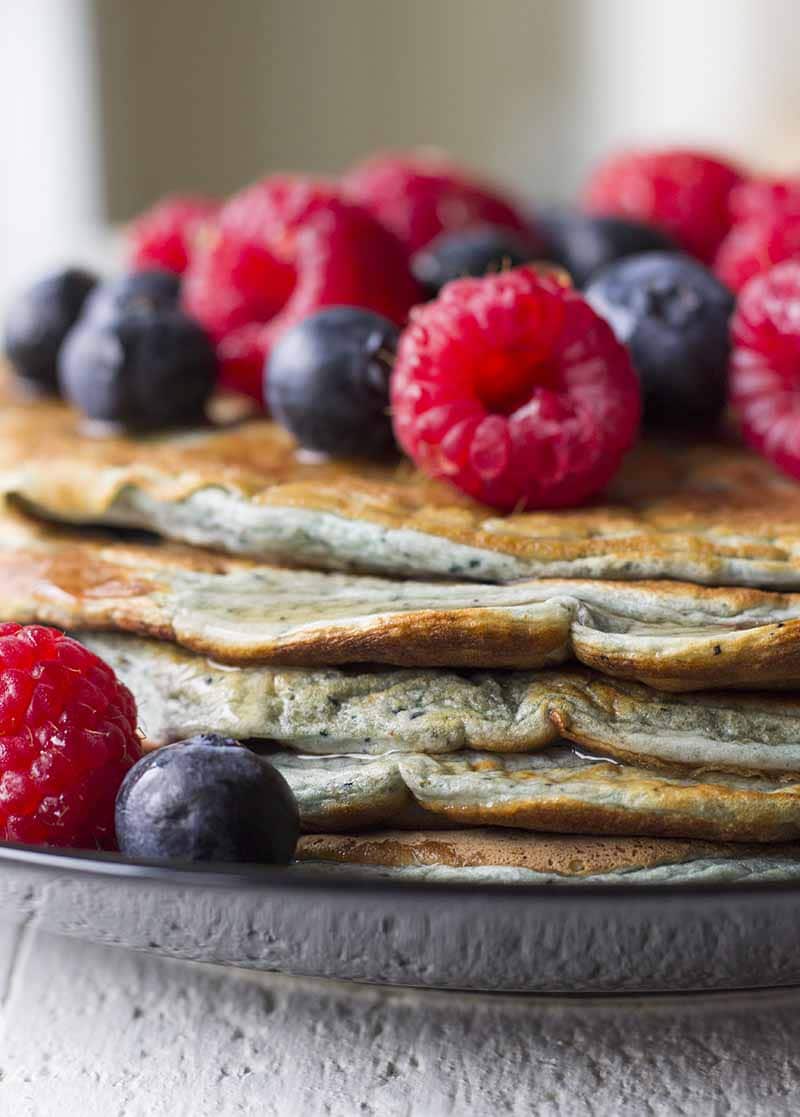 Une pile de crêpes protéinées sur une plaque noire avec des baies mélangées sur le dessus.